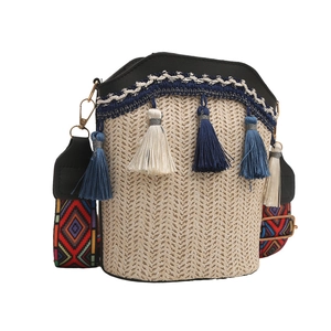 Close-up of woven straw bucket bag featuring blue tassels and a geometric fabric strap
