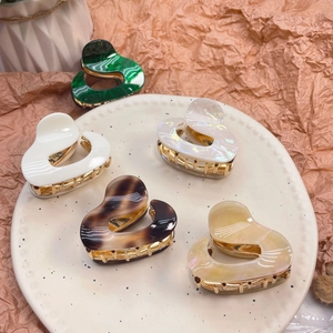 Detail view of colorful heart-shaped acetate hair claws on a ceramic dish