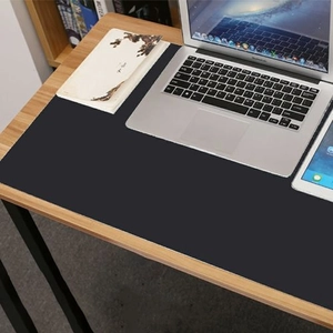 Close-up of a large black silicone desk mat with matte texture on a wooden table