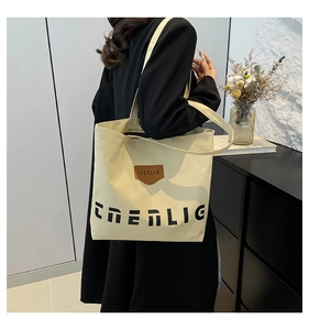 Detail view of large canvas tote bag with black letter print and brown leather patch