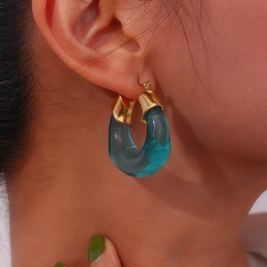 Fashionable gold metal U-shaped hoop earrings with transparent blue resin accents on a model