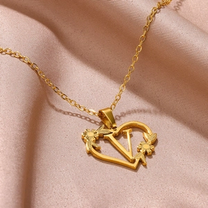 Dettaglio macro del ciondolo a cuore dorato con lettera V e incisione floreale