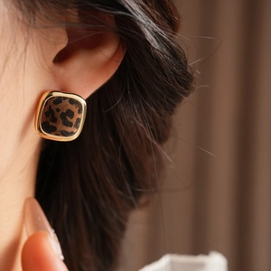 Detail of leopard print square earring with gold trim worn on the model's ear