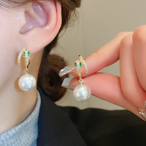 Close-up of golden snake earrings featuring sparkling diamonds and a white pearl drop