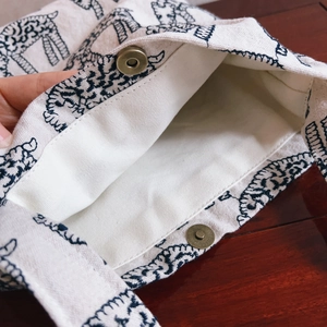 White canvas tote bag with blue animal embroidery and magnetic closure on wooden desk