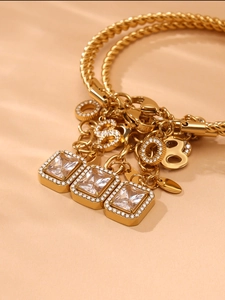 Macro detail of gold twist chain bracelet with square zircon pendants and pave-set charms