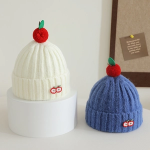 Close-up of knit hats with cute 3D apple pom-poms and cherry embroidery details