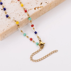 Minimalist gold necklace with colorful square beads on a decorative stone base