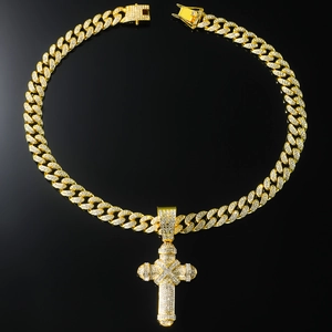 Gros plan sur un collier gourmette dorée avec un grand pendentif croix serti de cristaux