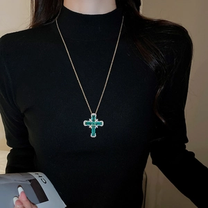 Détail d'un collier pendentif croix dorée avec zircon vert porté sur un mannequin en noir