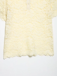 Close-up of pale yellow lace top featuring short sleeves and buttoned polo collar detail