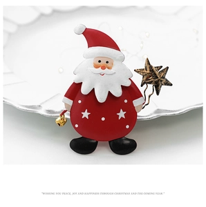 Macro shot of Santa Claus brooch with red enamel and gold bells on white plate