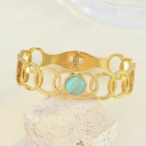 Macro detail of golden bracelet featuring light blue cat eye stone and hollow ring links