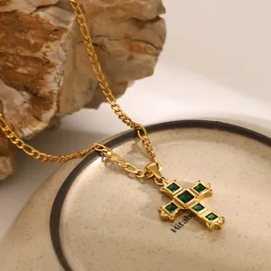 Macro detail of gold cross pendant with green emerald zircons on a Figaro chain