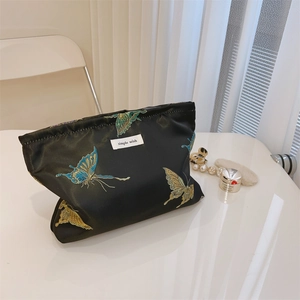 Detailed view of black satin cosmetic bag featuring colorful butterfly embroidery and logo