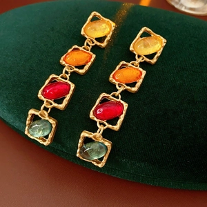 Detailansicht goldener Vintage-Ohrringe mit bunten Steinen auf grünem Samtkissen