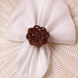 Close-up of brown woven rattan napkin ring with intricate knot on white fabric