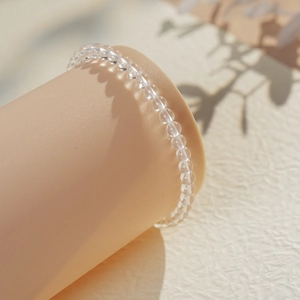 Detailed close-up of clear crystal beaded bracelet on a minimalist cylinder display