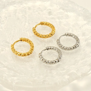 Detailed view of gold and silver textured hoop earrings on a decorative glass tray