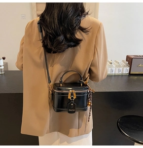 Detailed back view of a glossy black square crossbody bag with gold hardware worn by a model