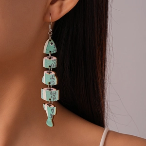 Close-up of a teal fish-shaped wooden drop earring worn by a model for vacation style