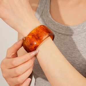 Detail shot of a retro amber resin wide bangle worn on a model wrist in natural light