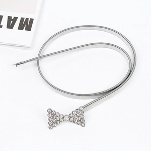 Détail d'une ceinture élastique en métal argenté avec boucle à nœud en strass brillant