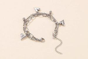 Detailed close-up of a silver double-layered heart chain bracelet on a warm beige background