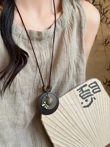 Detail of vintage wooden pendant necklace with bronze relief on a rustic linen dress