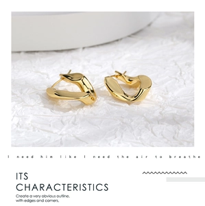 Macro shot of geometric egg-shaped gold earrings with sharp edges on white texture