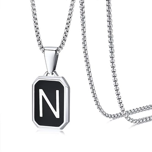 Macro detail of silver box chain necklace with black square pendant featuring letter N