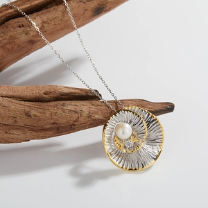 Detail of spiral disc necklace with pearl and zircon set against natural wood