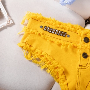 Dettaglio ravvicinato degli shorts in denim giallo con strass e orlo sfrangiato