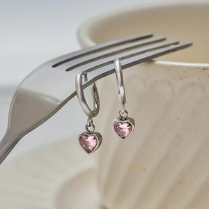 Macro shot of silver hoop earrings with pink heart-shaped crystal charms on a fork