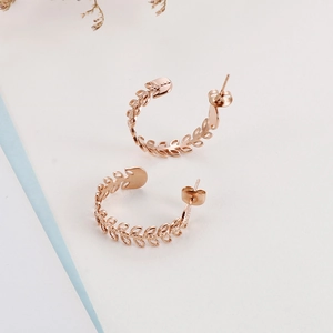 Makro-Detail von roségoldenen C-förmigen Ohrringen mit hohlem Olivenblatt-Design auf Weiß