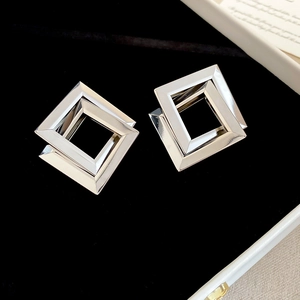 Macro detail of silver geometric interlocking square earrings on black velvet