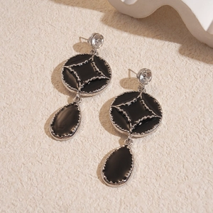 Macro detail of gothic style silver earrings with black enamel drop and star engraving