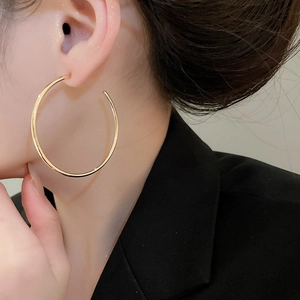 Close-up of a large gold polished C-shaped hoop earring worn by a model in formal attire