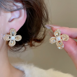 Détail de boucles d'oreilles fleurs plaquées or avec perle blanche et cristaux brillants