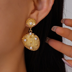 Detail of model wearing gold shell earrings with inlaid pearls in a luxury ocean style