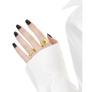 Layered gold rings with purple gemstone and ripple texture on model's hand with black nails