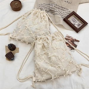 Close-up of beige canvas drawstring bag with decorative fringe texture on white fabric