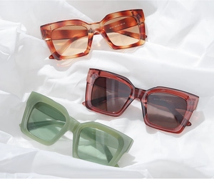 Three square oversized sunglasses in tortoiseshell, red, and green on white silk fabric