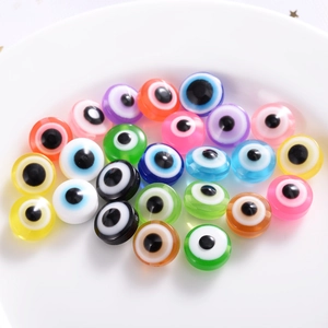 Flat lay of colorful resin evil eye flat round beads scattered in a white decorative tray