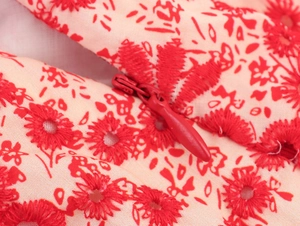 Detail van rood bloemenborduurwerk op abrikozenstof met een onzichtbare ritssluiting