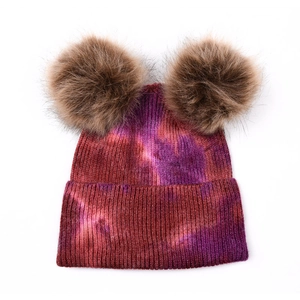 Détail du bonnet en tricot tie-dye avec deux grands pompons en fausse fourrure marron