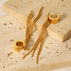 Detailed close-up of golden stainless steel hoop earrings with ball chain tassels on stone