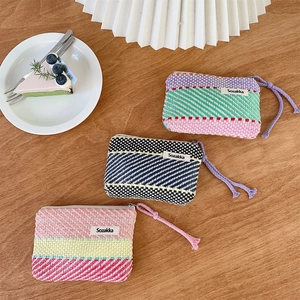 Flat lay of colorful woven makeup pouches with metal zippers on a wooden table