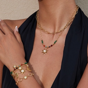 Close-up of layered gold necklace and bracelets with sun, moon, and bead charms