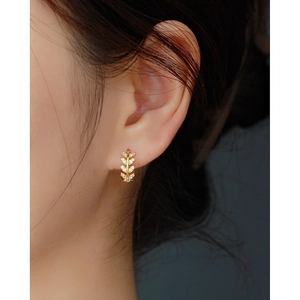 Close-up of a gold leaf-shaped hoop earring with diamonds on a model's ear